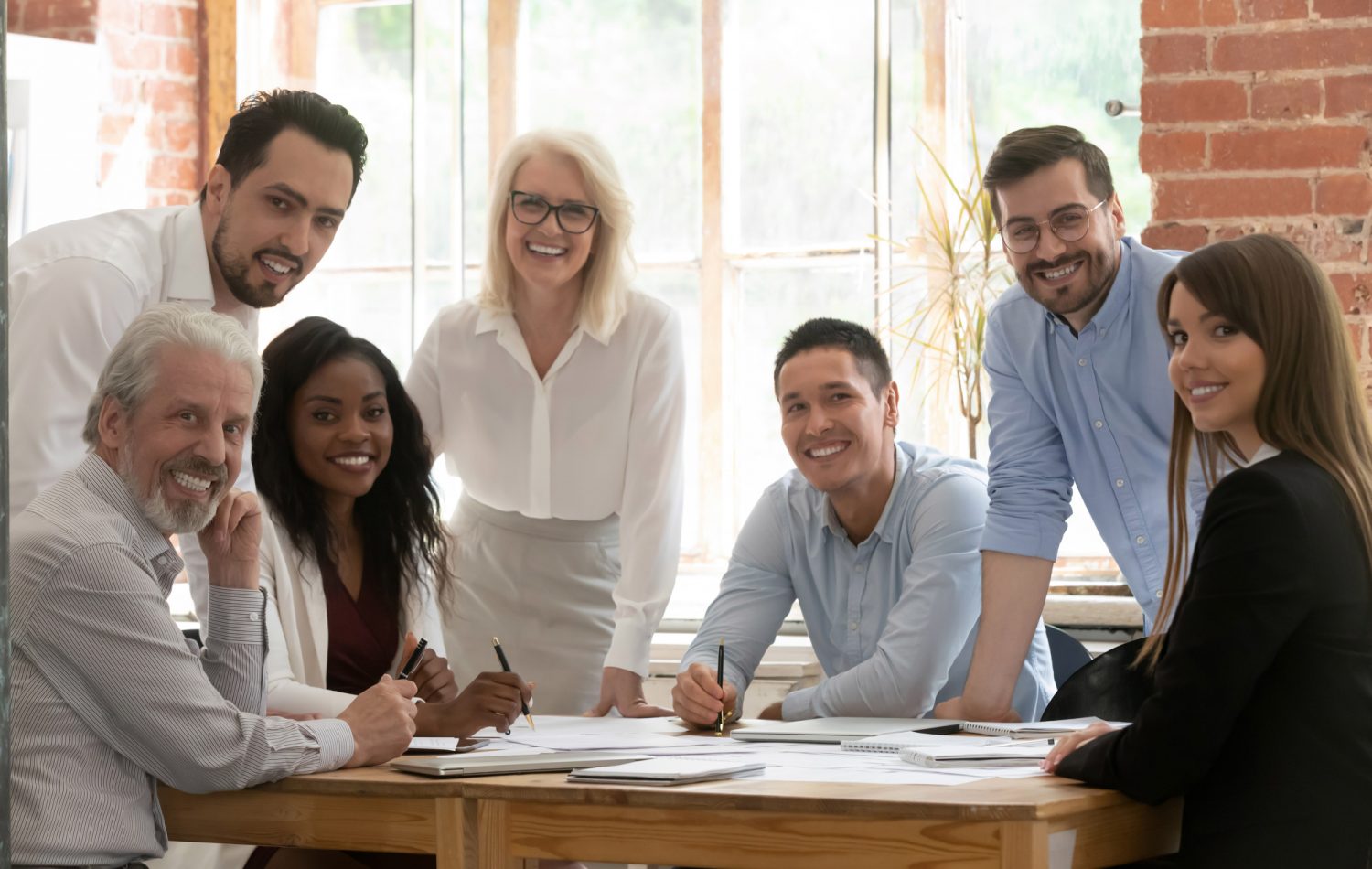 Professional business team young and old people posing together at office table, happy diverse leaders employees looking at camera, smiling multiracial staff corporate people workers group portrait